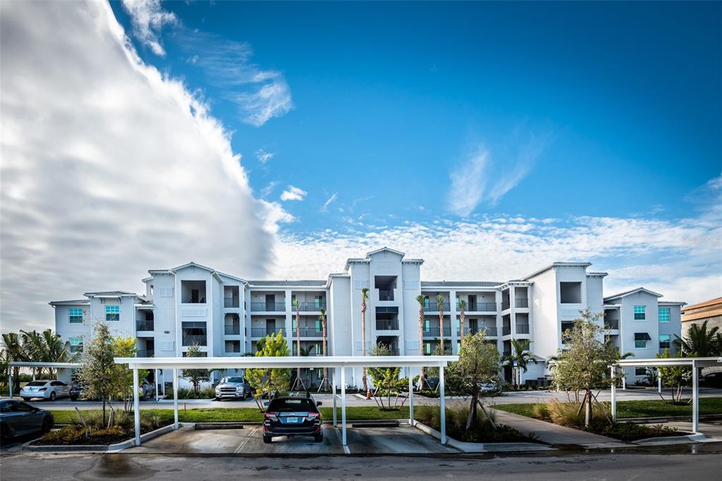 A multi-story apartment building features white stucco walls, balconies, and covered parking spaces in front — 14051 HERITAGE LANDING BOULEVARD UNIT 511, PUNTA GORDA, FL