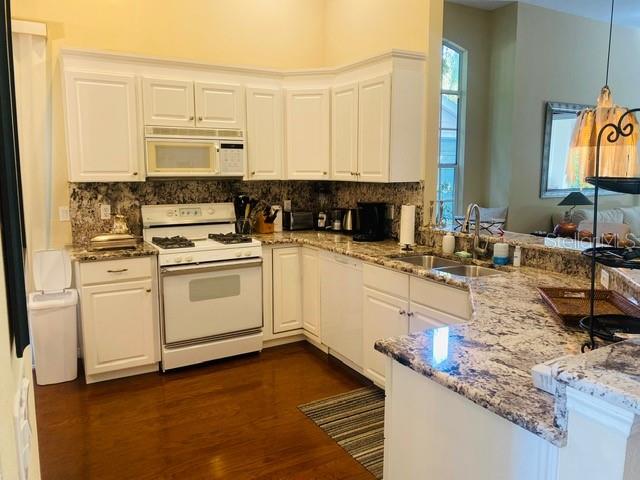 A kitchen features white cabinets, granite countertops, stainless steel appliances, and dark hardwood flooring — 7711 WHITEBRIDGE GLEN, UNIVERSITY PARK, FL