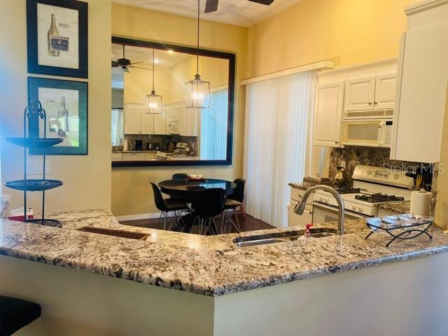 A kitchen with granite countertops, white cabinets, and a dining area reflected in a mirror — 7711 WHITEBRIDGE GLEN, UNIVERSITY PARK, FL