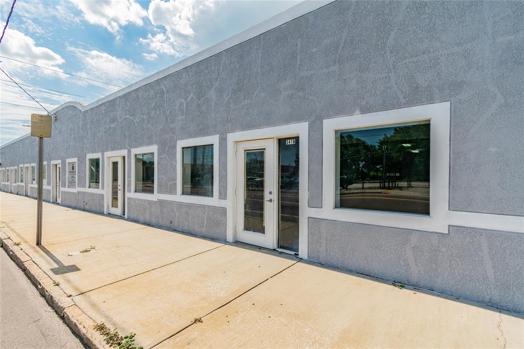 A gray commercial building exterior features multiple glass doors and windows along a concrete sidewalk — 3410 E 7TH AVENUE, TAMPA, FL