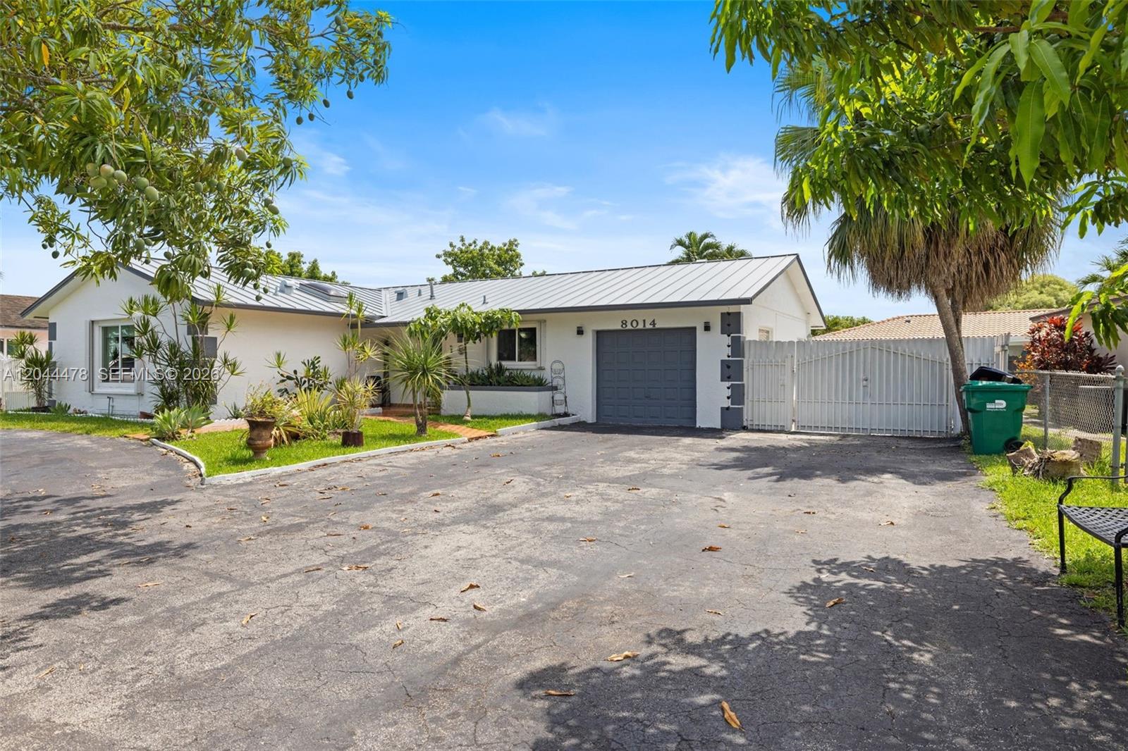 A single-story house with a metal roof, gray garage door, and a large asphalt driveway — 8014 SW 133rd Ct, Miami FL 33183, MIAMI, FL