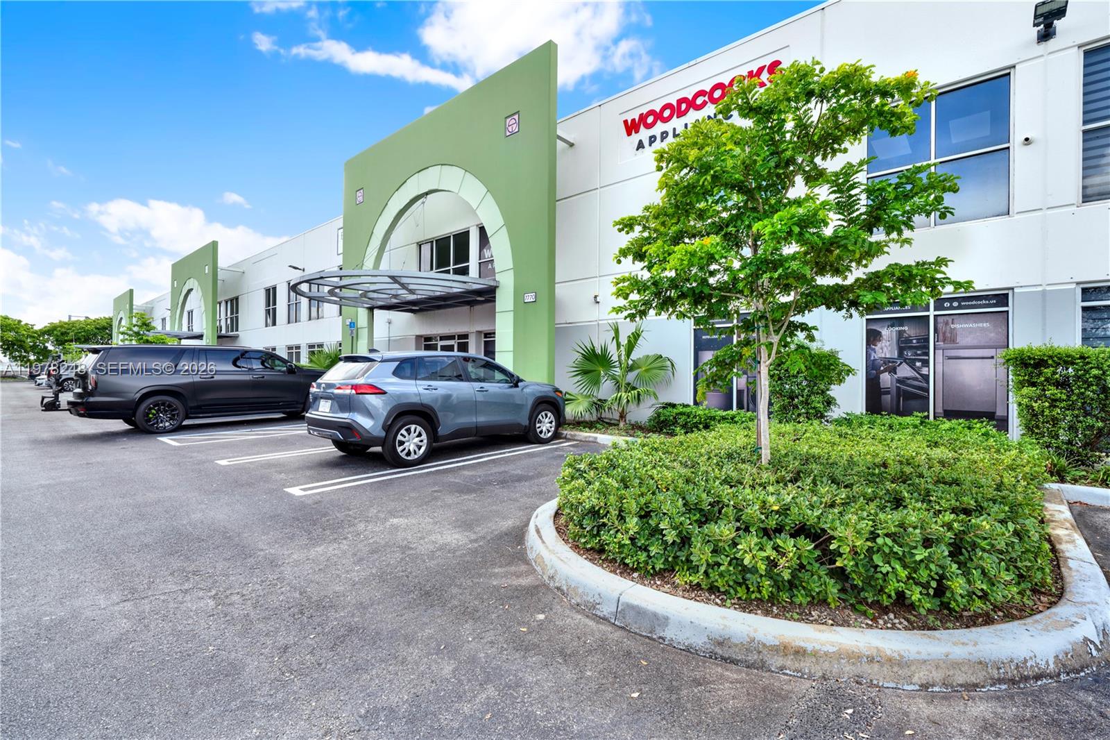 A gray SUV is parked in front of a commercial building with green arched entrances — 7770 NW 46th St # 23, Doral FL 33166, DORAL, FL