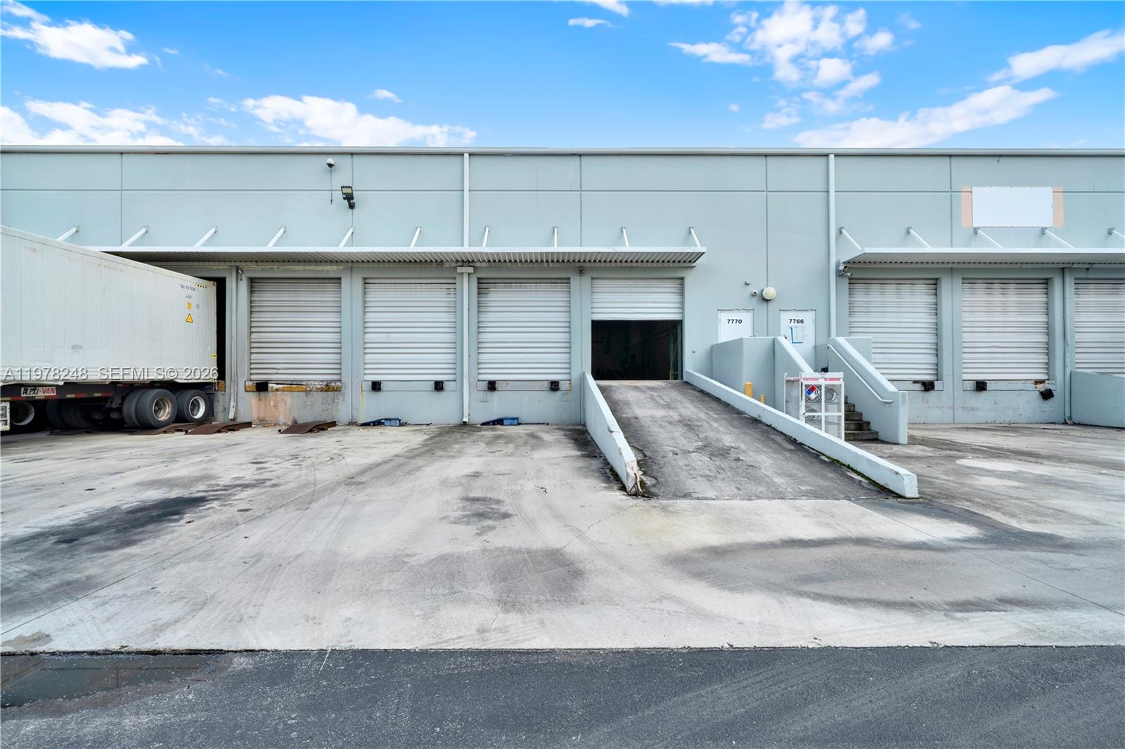 The exterior of a warehouse building features multiple loading dock doors and a concrete ramp — 7770 NW 46th St # 23, Doral FL 33166, DORAL, FL