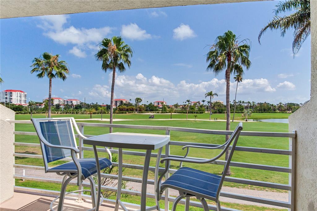A balcony with a small table and two chairs overlooks a golf course and palm trees — 6171 BAHIA DEL MAR BOULEVARD UNIT 216, ST PETERSBURG, FL