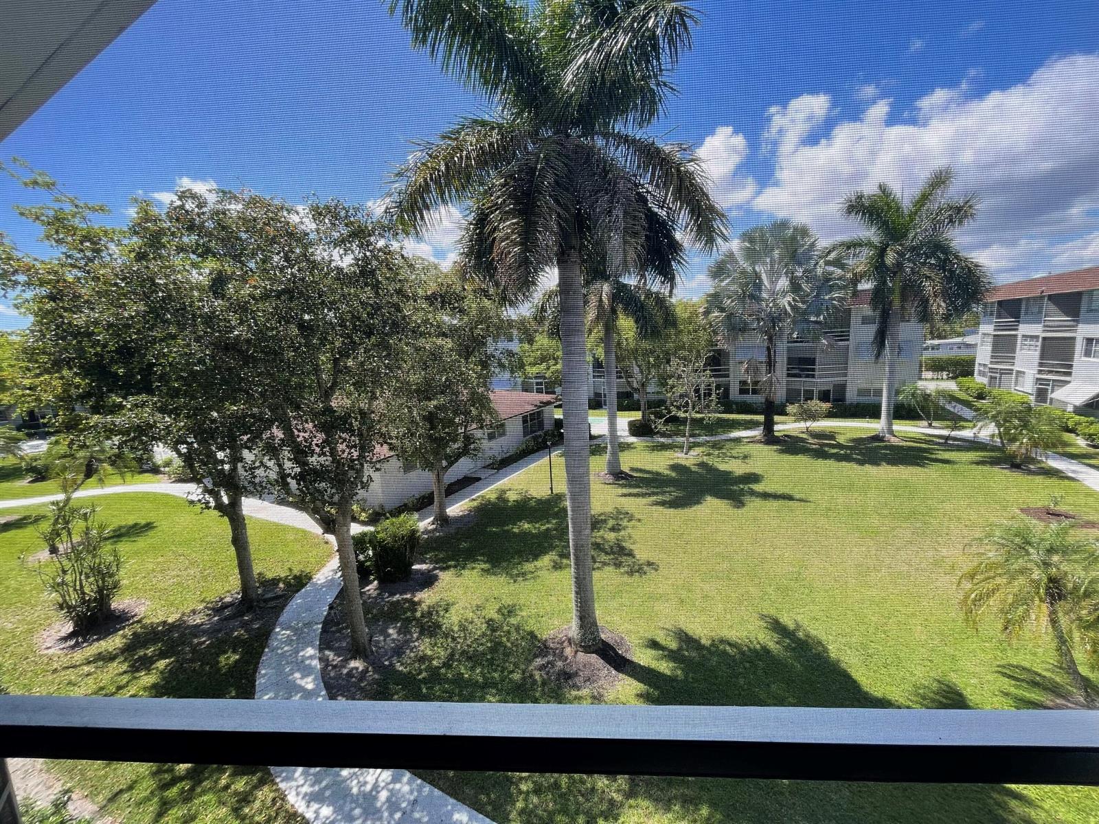 A view from a screened balcony overlooking a grassy courtyard with palm trees and walkways — 400 SE 10th Street # 308, Deerfield Beach FL 33441, DEERFIELD BEACH, FL