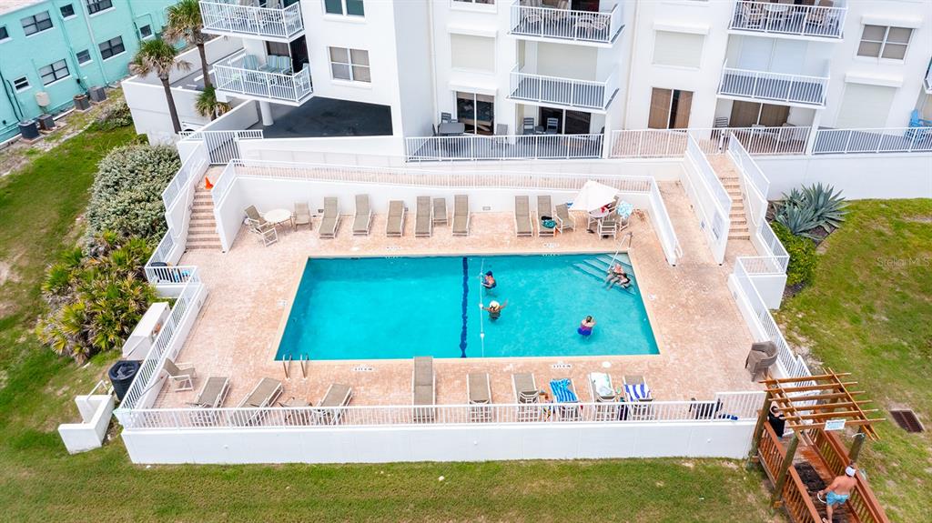 An aerial view shows a rectangular swimming pool surrounded by a patio and white fencing — 1183 OCEAN SHORE BOULEVARD UNIT 604, ORMOND BEACH, FL