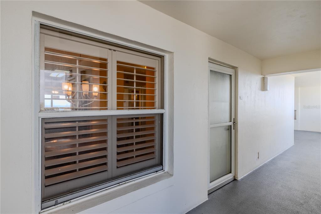 A white exterior hallway features a window with shutters and a glass storm door — 1183 OCEAN SHORE BOULEVARD UNIT 604, ORMOND BEACH, FL