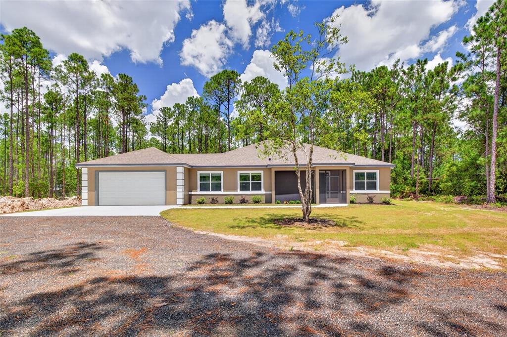 A single-story tan house with a two-car garage sits in a wooded lot — 5390 MAHOGANY BOULEVARD, BUNNELL, FL