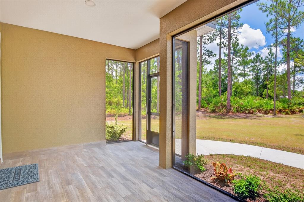 A covered patio with light wood-look tile flooring, screen walls, and a view of trees — 5390 MAHOGANY BOULEVARD, BUNNELL, FL