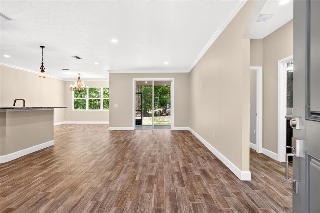 An open-concept living area features wood-look tile flooring, neutral walls, and sliding glass patio doors — 5390 MAHOGANY BOULEVARD, BUNNELL, FL