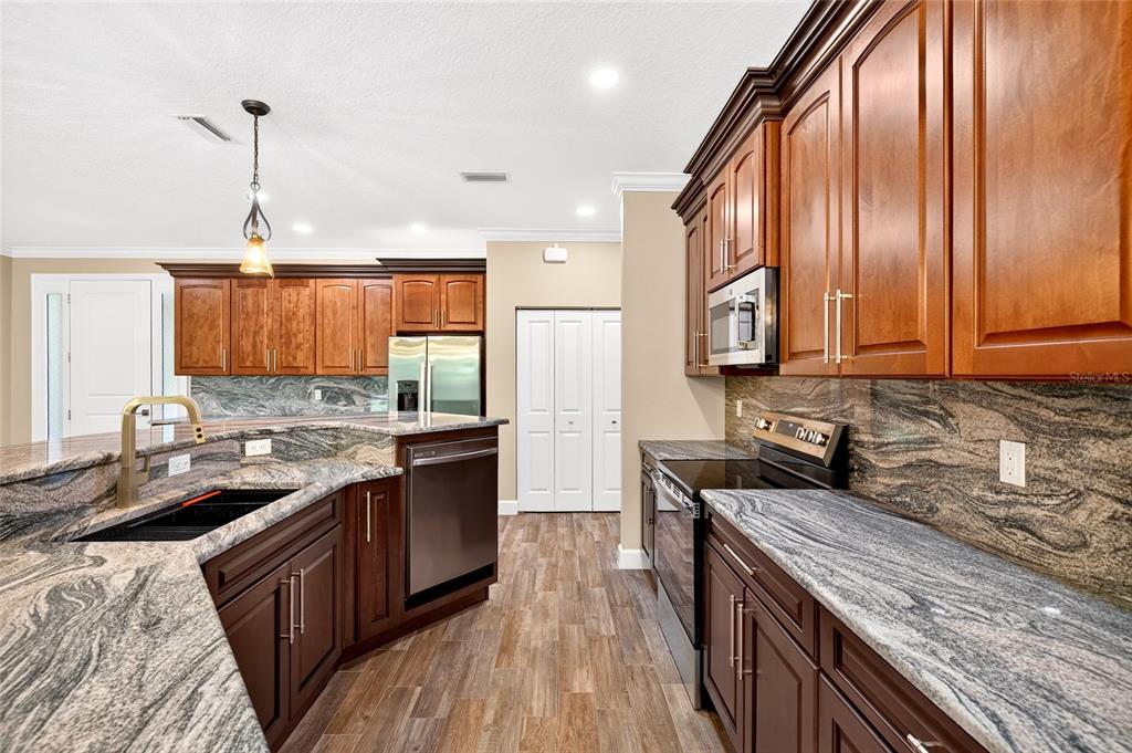 A kitchen features dark wood cabinets, granite countertops, stainless steel appliances, and wood-look flooring — 5390 MAHOGANY BOULEVARD, BUNNELL, FL