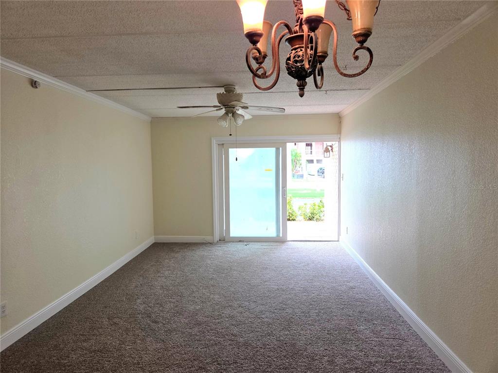 An empty living room features beige carpet, a ceiling fan, a chandelier, and sliding glass doors — 10365 PARADISE BOULEVARD UNIT 13, TREASURE ISLAND, FL