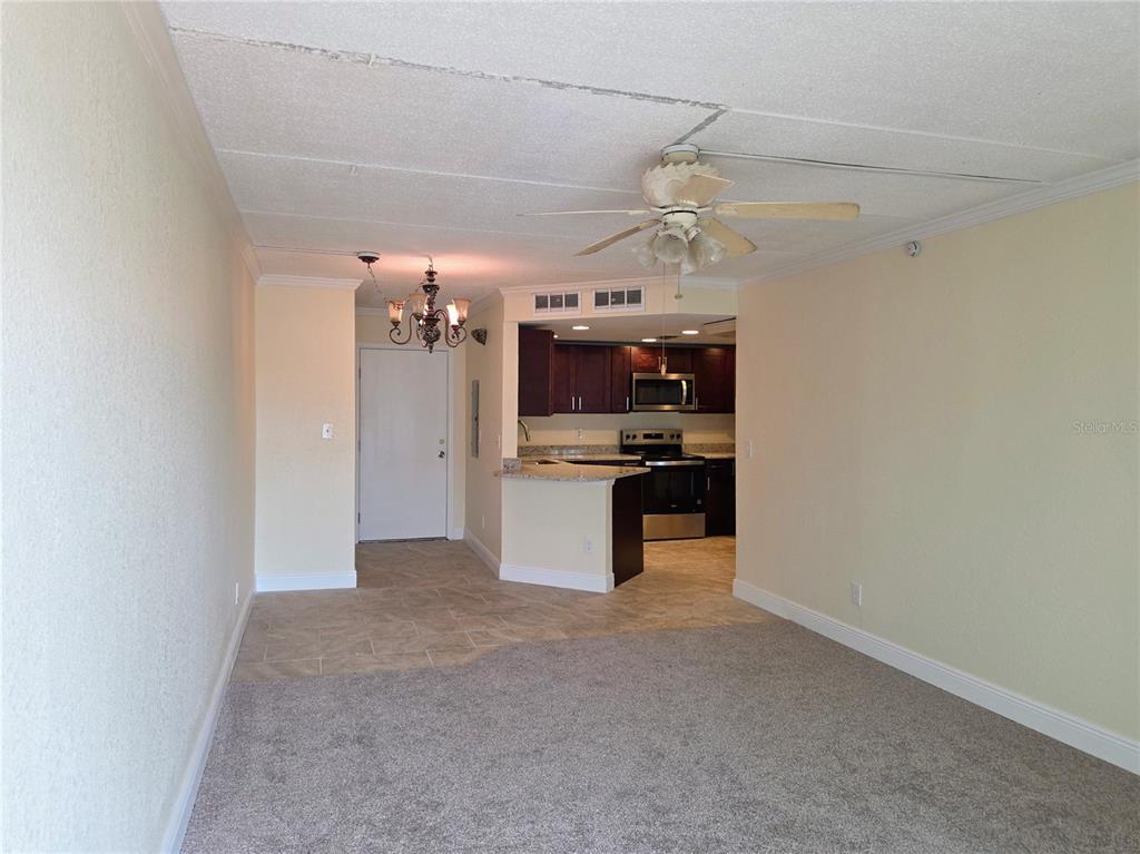 An open-concept living area features carpeted flooring, a ceiling fan, and an adjacent kitchen — 10365 PARADISE BOULEVARD UNIT 13, TREASURE ISLAND, FL
