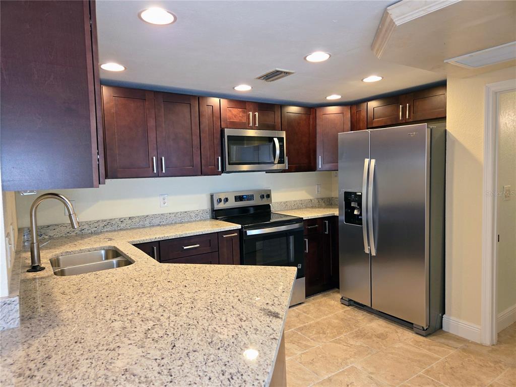 A kitchen featuring dark wood cabinets, granite countertops, and stainless steel appliances — 10365 PARADISE BOULEVARD UNIT 13, TREASURE ISLAND, FL
