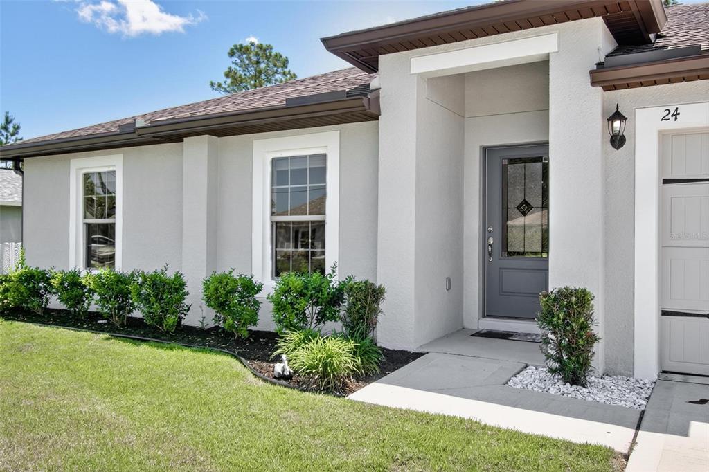 The exterior of a light-colored house features a gray front door and a garage — 24 PERKINS LANE, PALM COAST, FL