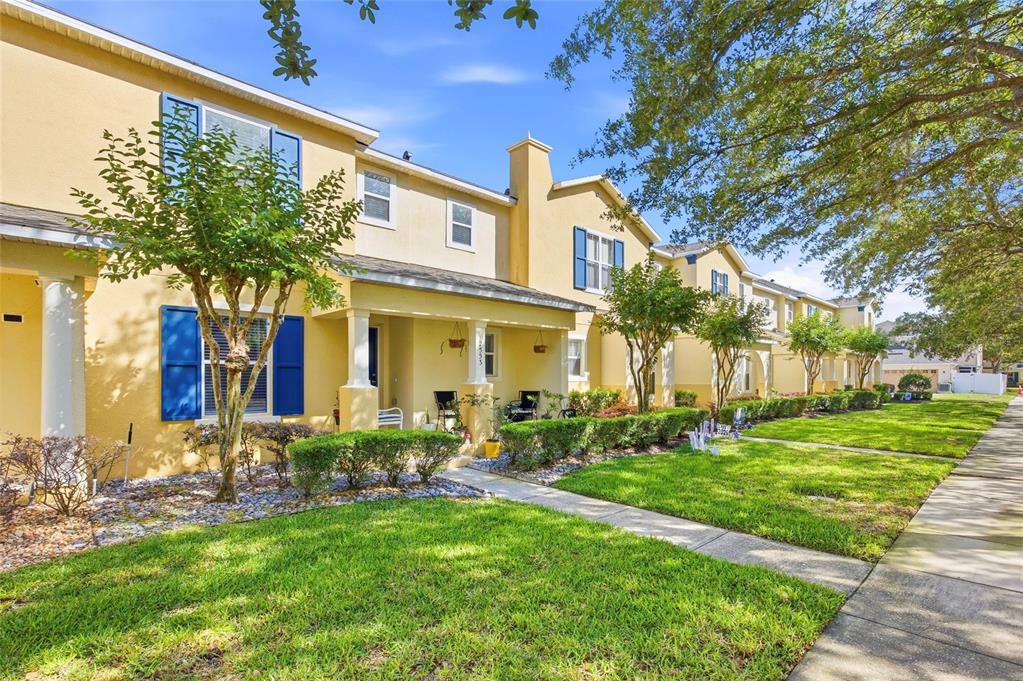 A row of yellow two-story townhomes with blue shutters and front porches along a sidewalk — 2553 ABEY BLANCO DRIVE, ORLANDO, FL