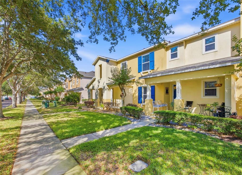 A two-story yellow townhouse with blue shutters and a covered front porch sits beside a sidewalk — 2553 ABEY BLANCO DRIVE, ORLANDO, FL