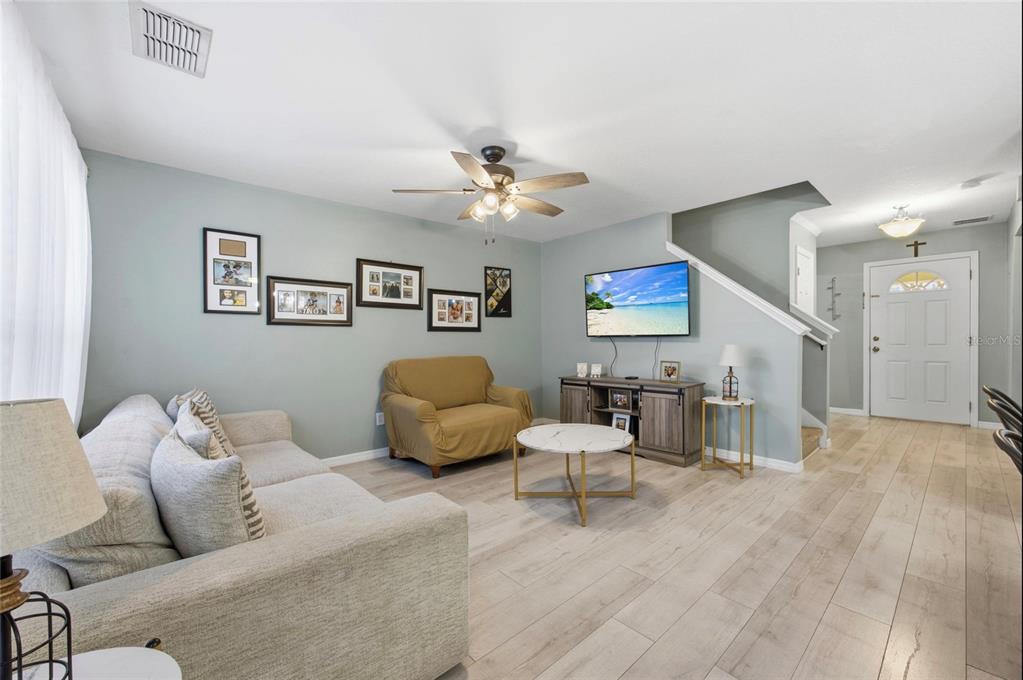 A living room features light wood flooring, a grey sofa, a tan armchair, and a television — 2553 ABEY BLANCO DRIVE, ORLANDO, FL