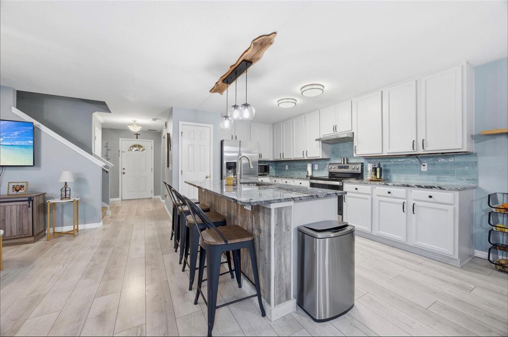 A kitchen with white cabinets, a granite-topped island, and light wood-look flooring — 2553 ABEY BLANCO DRIVE, ORLANDO, FL
