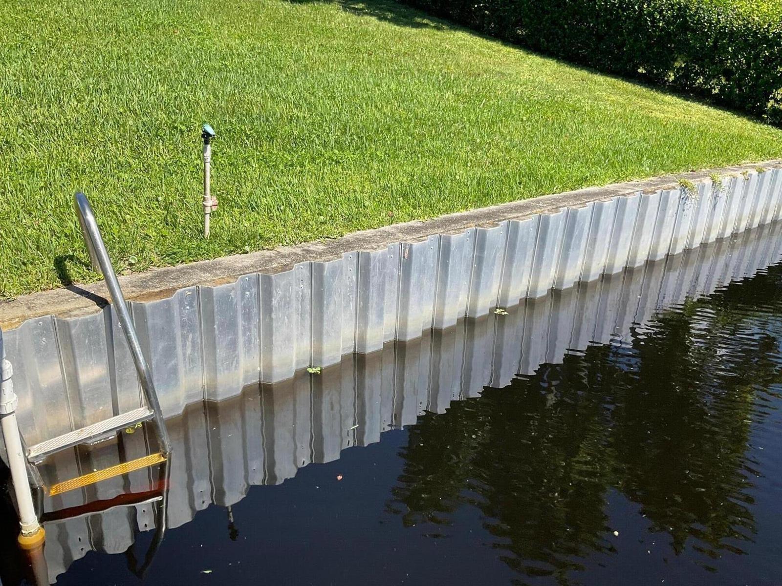 A metal seawall borders a grassy lawn next to a canal with a pool ladder — 2508 SE 32nd Street, Okeechobee FL 34974, OKEECHOBEE, FL