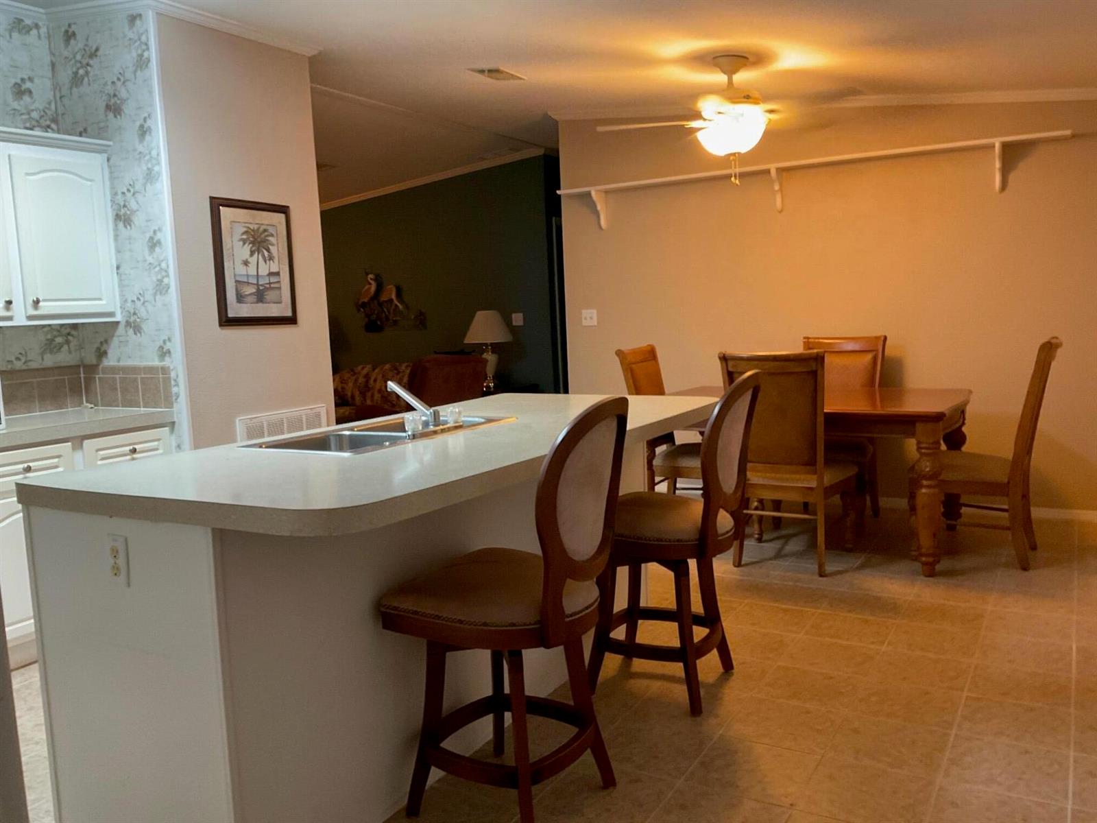 A kitchen island with a sink and bar stools sits before a dining area — 2508 SE 32nd Street, Okeechobee FL 34974, OKEECHOBEE, FL