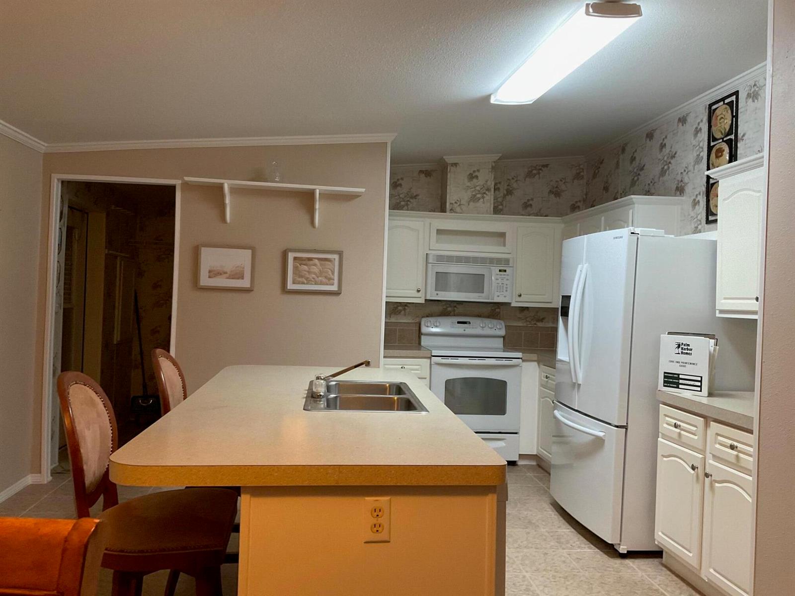 A kitchen features white cabinets, a central island with a sink, and white appliances — 2508 SE 32nd Street, Okeechobee FL 34974, OKEECHOBEE, FL