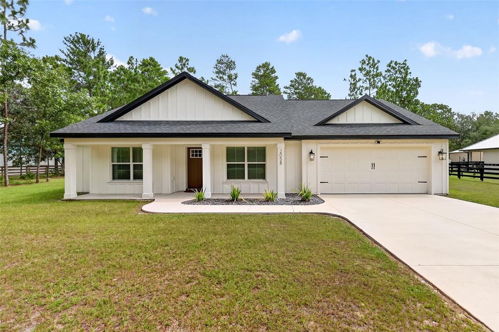 A single-story white house with a black roof, front porch, and attached two-car garage — 2058 COUNTY ROAD 243F, WILDWOOD, FL