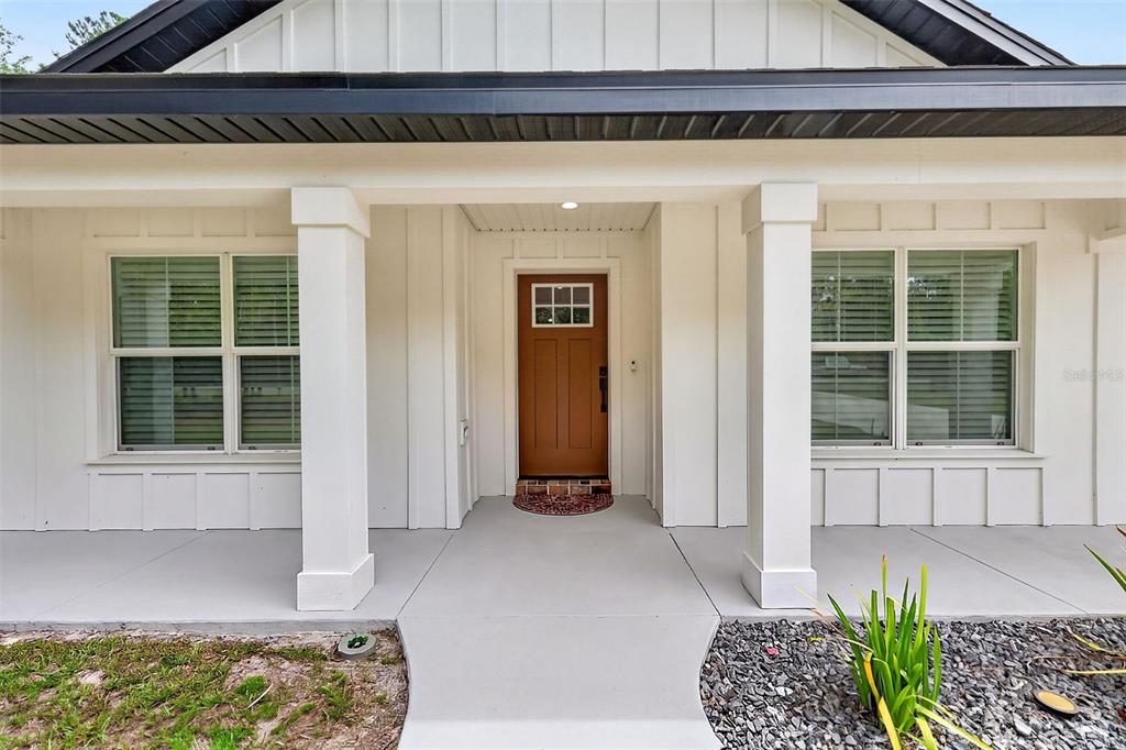 A front porch with white columns leads to a brown door on a house exterior — 2058 COUNTY ROAD 243F, WILDWOOD, FL
