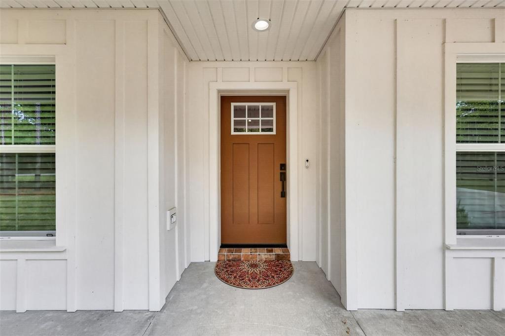 A front porch features a brown door with a window and white board-and-batten siding — 2058 COUNTY ROAD 243F, WILDWOOD, FL