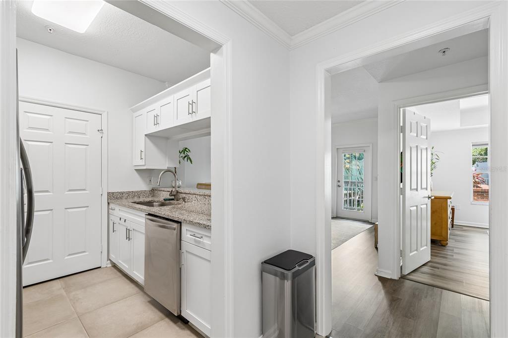 A kitchen with white cabinets, granite countertops, and stainless steel appliances leads to a hallway — 800 S DAKOTA AVENUE UNIT 237, TAMPA, FL