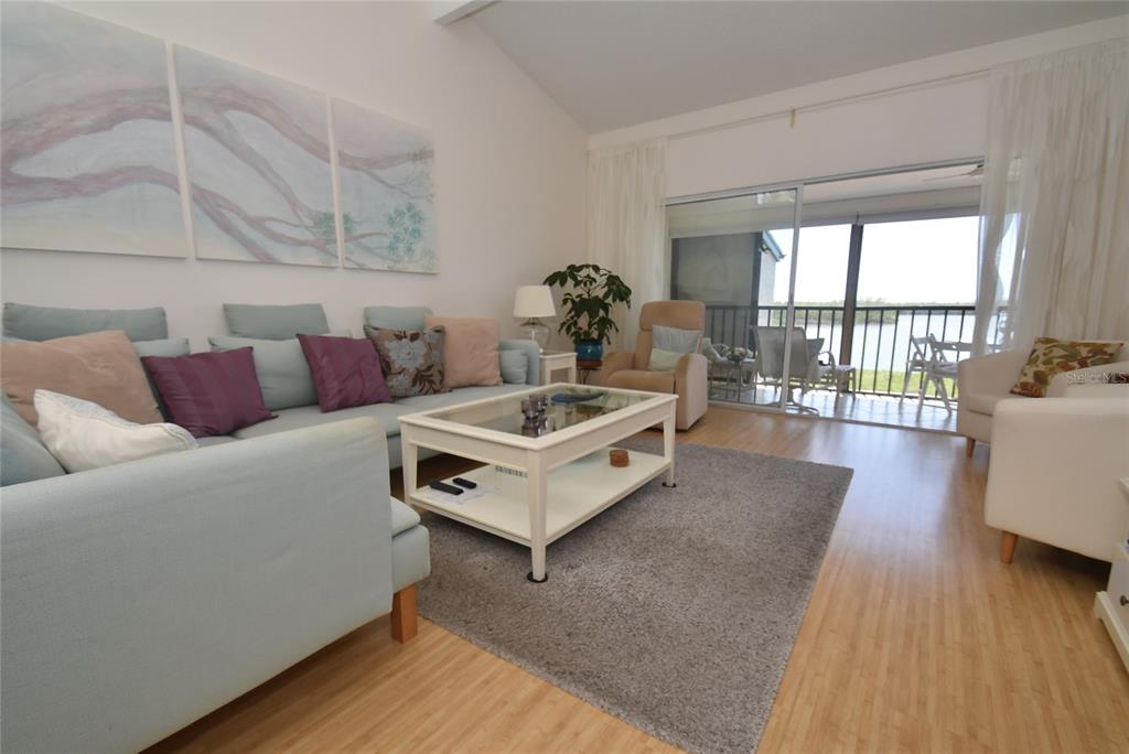 A living room features a light blue sofa, a coffee table, and a balcony view — 1512 PELICAN POINT DRIVE UNIT BA264, SARASOTA, FL