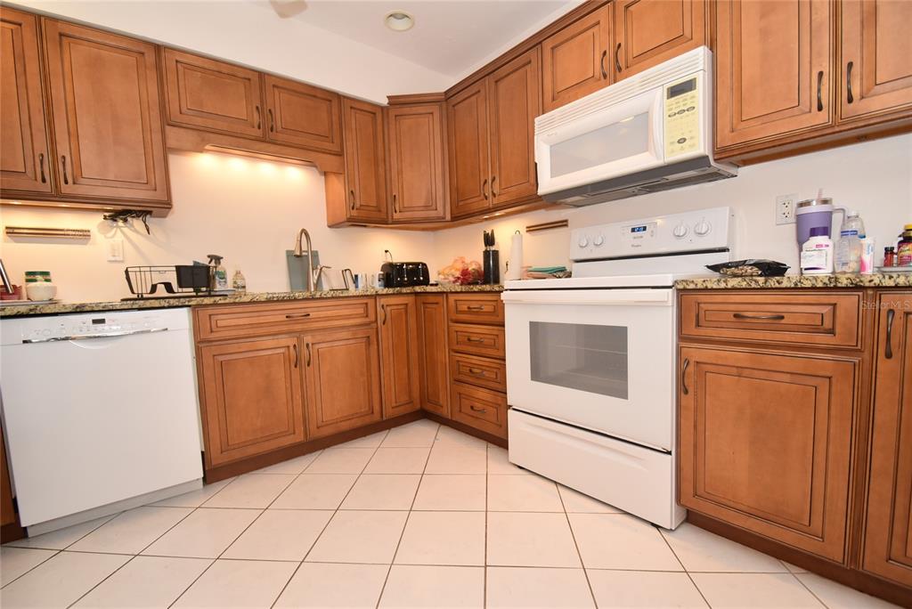 A kitchen features wood cabinets, granite countertops, white appliances, and light-colored tile flooring — 1512 PELICAN POINT DRIVE UNIT BA264, SARASOTA, FL