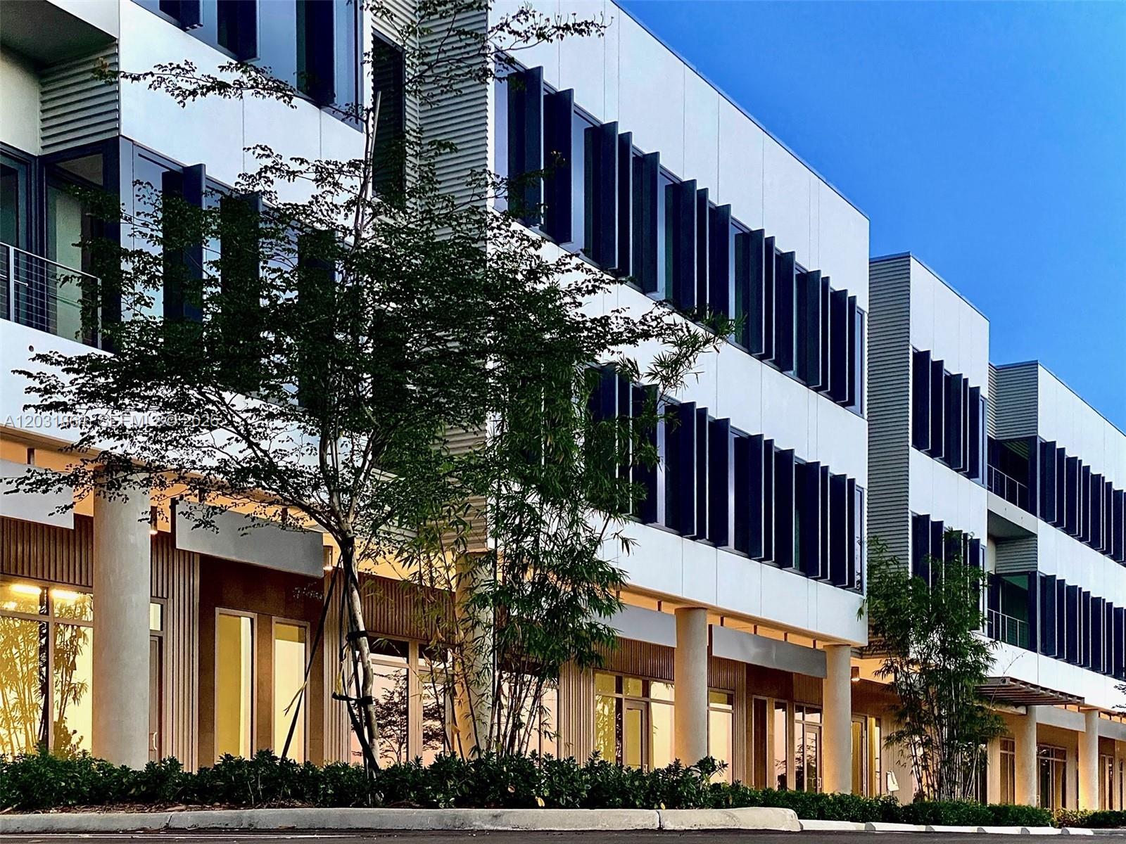 A modern multi-story office building features white panels, vertical window louvers, and ground-level glass storefronts — SWEETWATER, FL