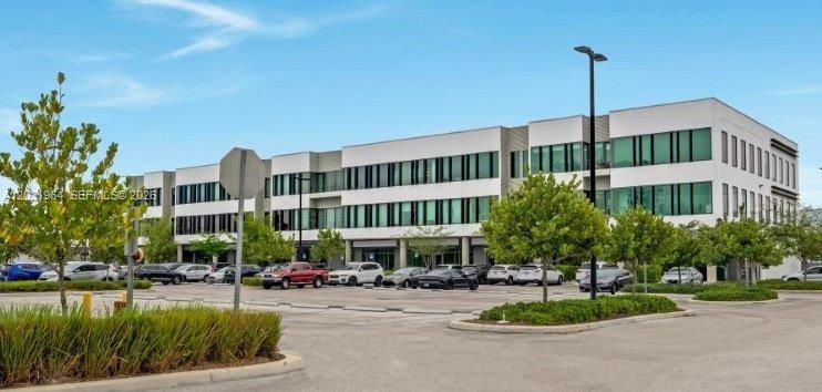 A multi-story commercial office building with a large parking lot in the foreground — SWEETWATER, FL