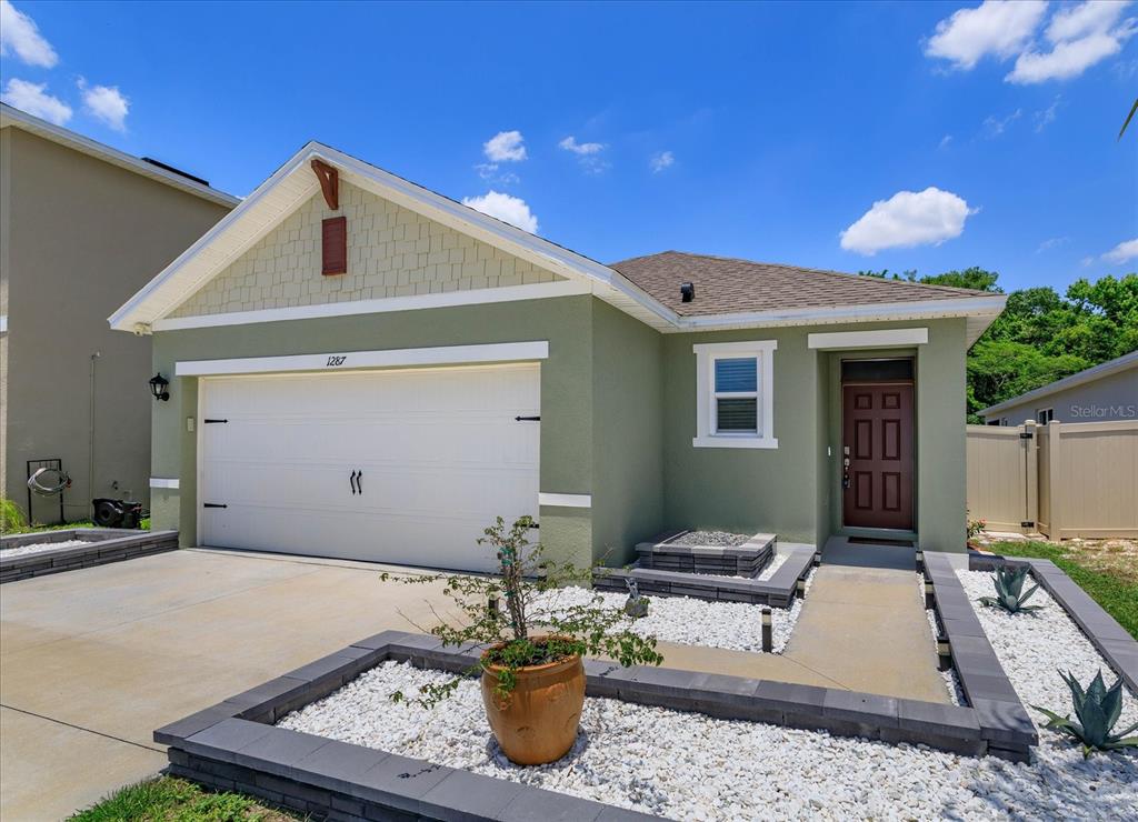A single-story house with green stucco siding, a white garage door, and a landscaped front yard — 1287 BERRY LANE, DAVENPORT, FL