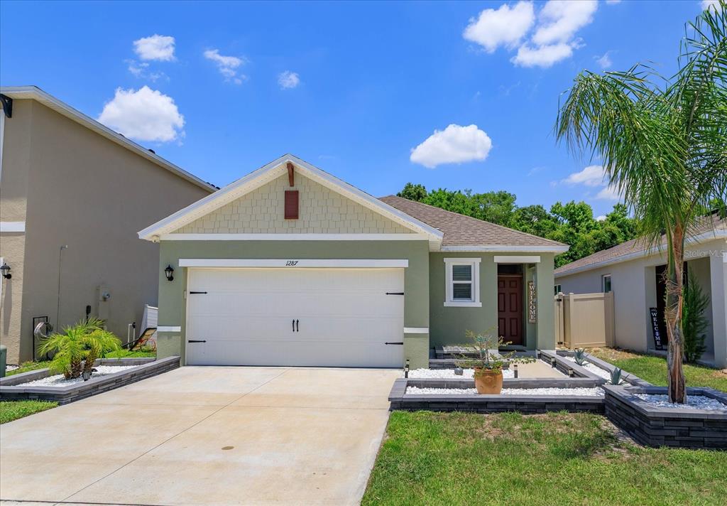 A single-story house with a green exterior, a two-car garage, and a landscaped front yard — 1287 BERRY LANE, DAVENPORT, FL