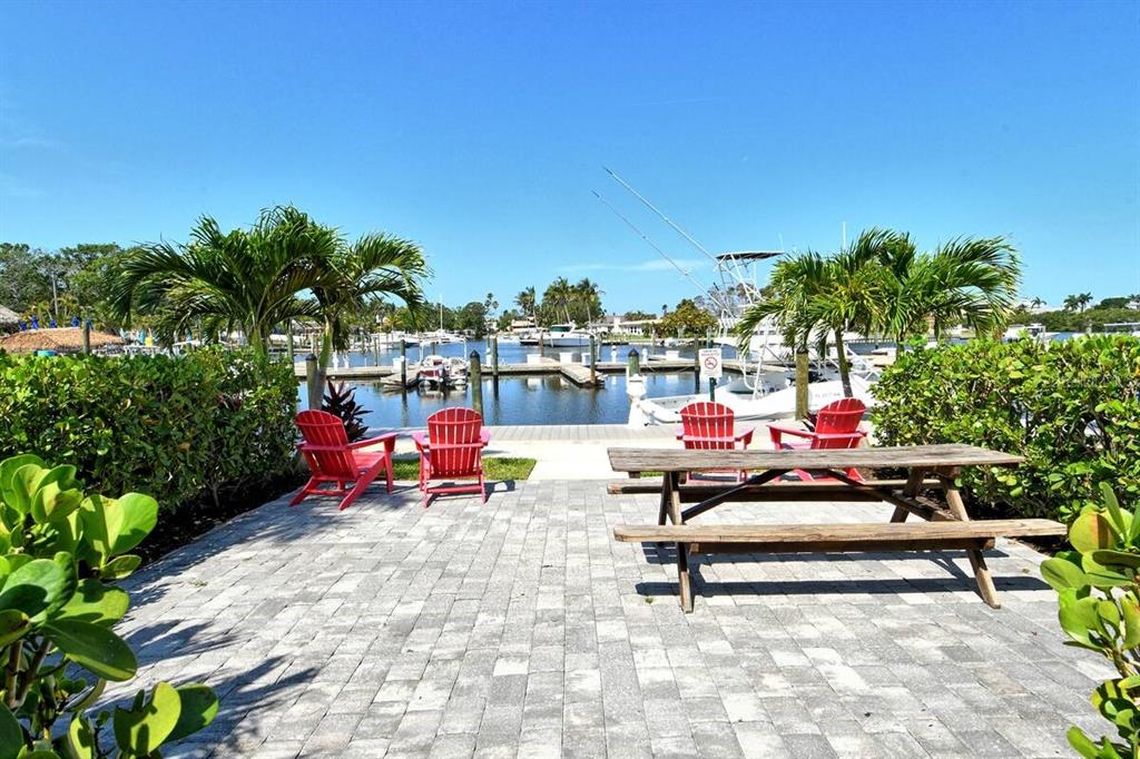 A paved patio features a wooden picnic table and red chairs overlooking a boat marina — 7150 N TAMIAMI TRAIL UNIT S-612, SARASOTA, FL