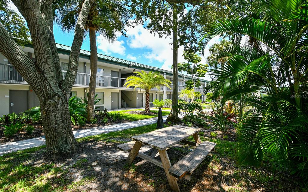 A wooden picnic table sits on a grassy lawn in front of a multi-story apartment building — 7150 N TAMIAMI TRAIL UNIT S-612, SARASOTA, FL