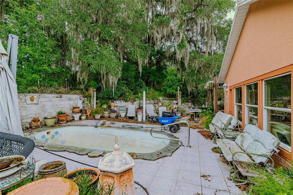 A backyard patio features a small, empty swimming pool, outdoor furniture, and a stone wall — 8845 NW 130TH STREET, REDDICK, FL