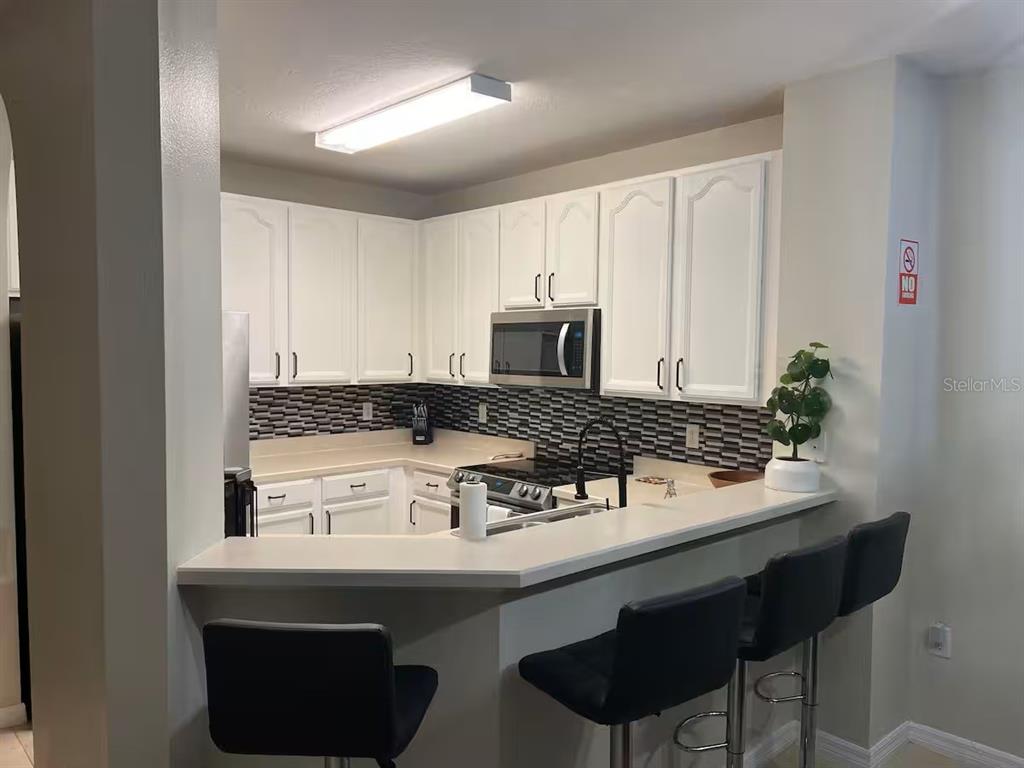 A kitchen features white cabinets, a dark tiled backsplash, stainless steel appliances, and a breakfast bar — 326 CHELSEA DRIVE, DAVENPORT, FL