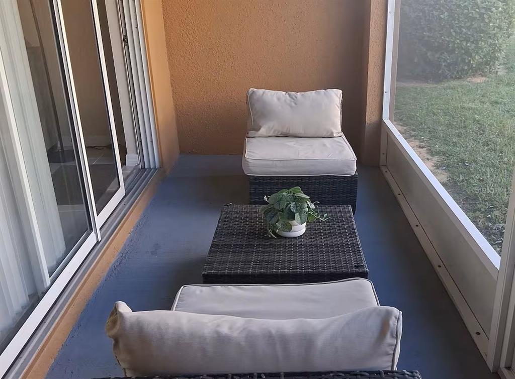 A screened-in patio features wicker furniture with light cushions and a small potted plant — 326 CHELSEA DRIVE, DAVENPORT, FL