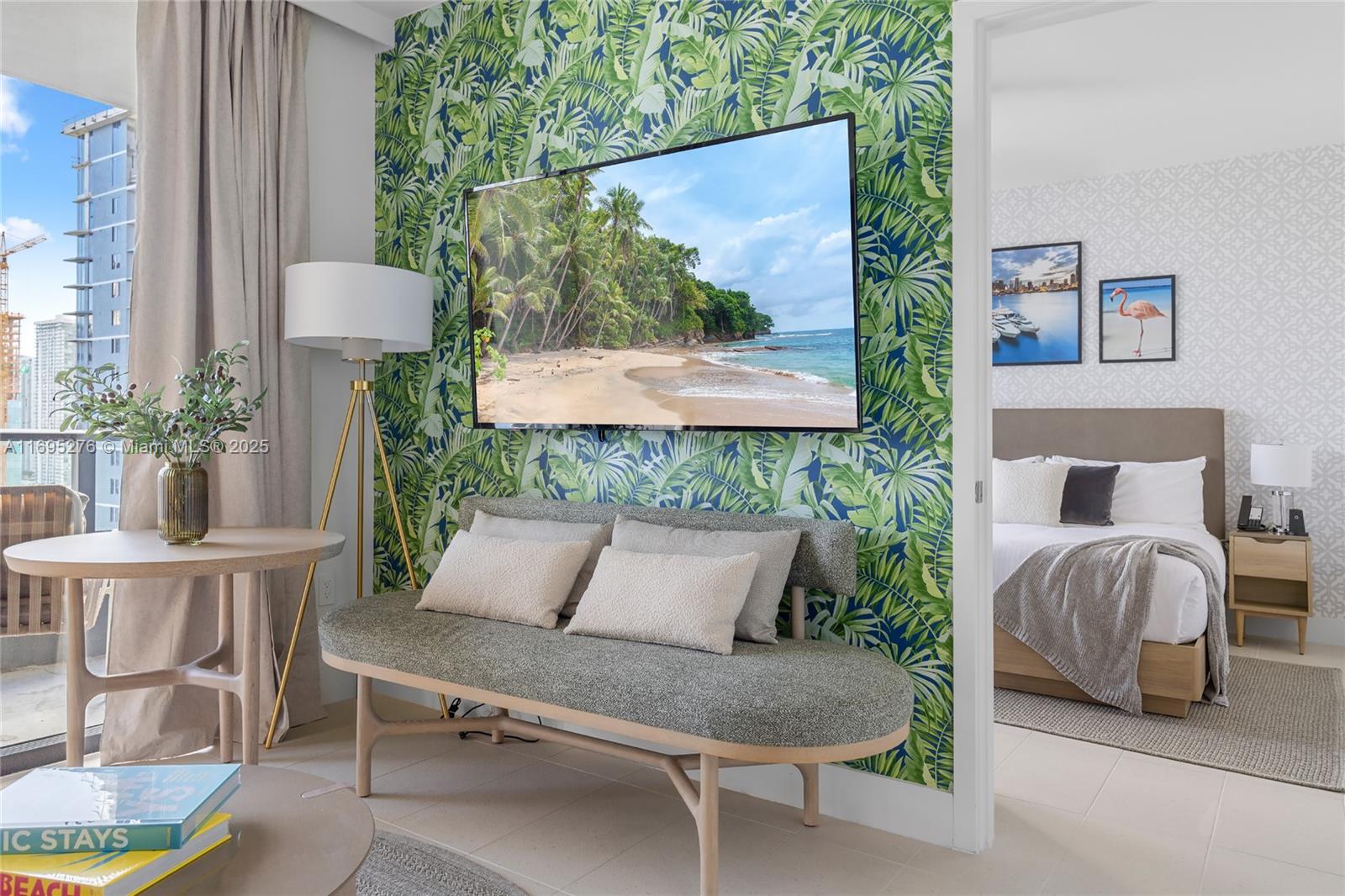 A living area with a tropical wallpaper accent wall, a television, and a bedroom beyond — 159 NE 6TH ST # 2414, Miami FL 33132, MIAMI, FL