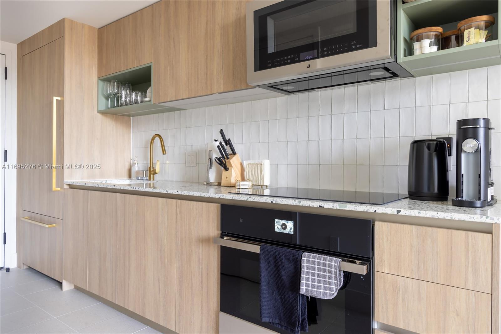 A modern kitchen features light wood cabinetry, white tile backsplash, and a speckled stone countertop — 159 NE 6TH ST # 2414, Miami FL 33132, MIAMI, FL