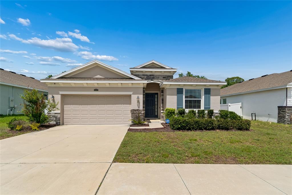 A single-story house with a beige stucco exterior, stone accents, and a two-car garage — 35977 MORSE WILLOW COURT, ZEPHYRHILLS, FL