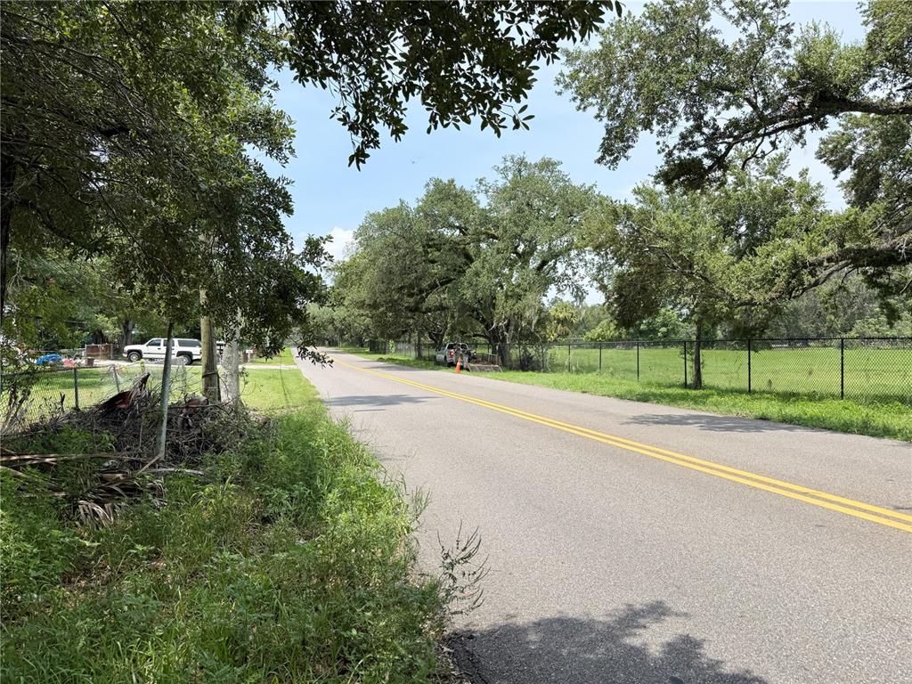 A paved road stretches into the distance, flanked by trees and a chain-link fence — 4621 E LAKE AVE, TAMPA, FL