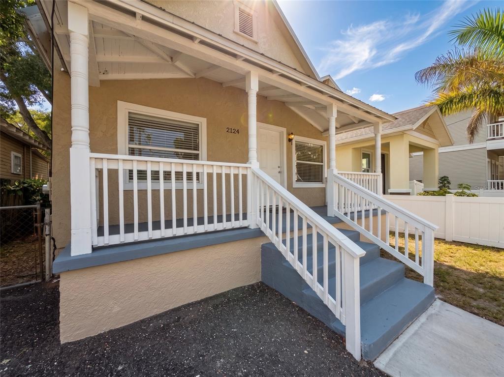 A tan house features a white-railed front porch with gray steps and a gravel yard — 2124 W CHESTNUT STREET, TAMPA, FL