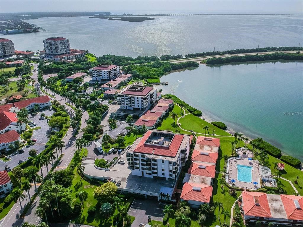 An aerial view shows waterfront condominium buildings with red tile roofs and a swimming pool — 6365 BAHIA DEL MAR BOULEVARD UNIT 210, ST PETERSBURG, FL