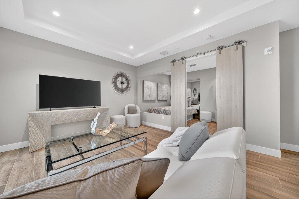 A modern living room features a wall-mounted television, glass coffee table, and sliding barn doors — 41 SW Seminole Street # 304, Stuart FL 34994, STUART, FL