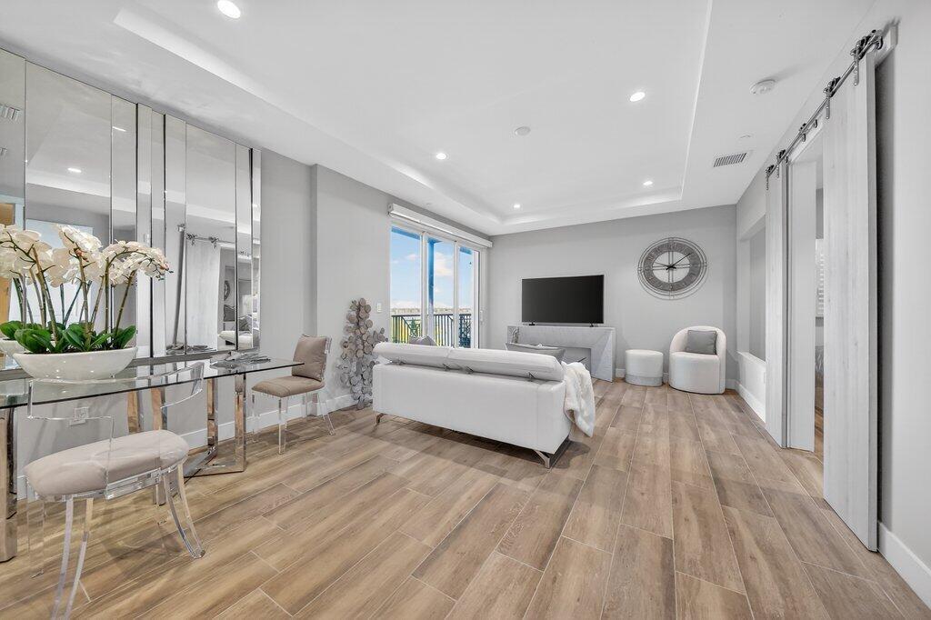 A modern living room features light wood-look tile floors, a white sofa, and mirrored walls — 41 SW Seminole Street # 304, Stuart FL 34994, STUART, FL