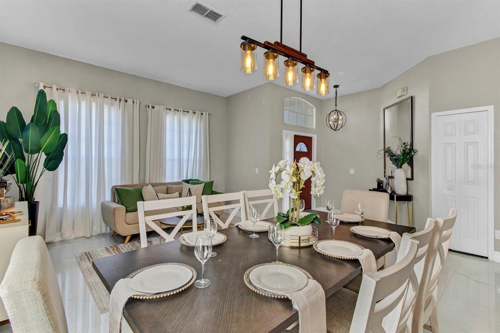 A dining room features a dark wood table, white chairs, and a modern linear chandelier — 256 CORK WAY, DAVENPORT, FL